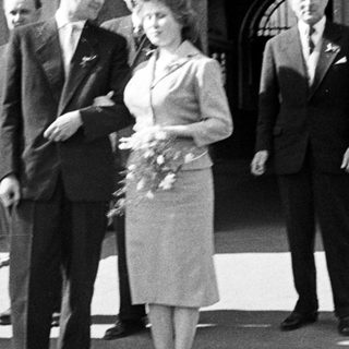Couple exits building, surrounded by men, in vintage attire.
