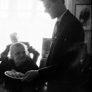 Man serves food to seated people at a table.