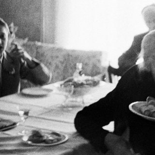Man serves food to seated people at a table.
