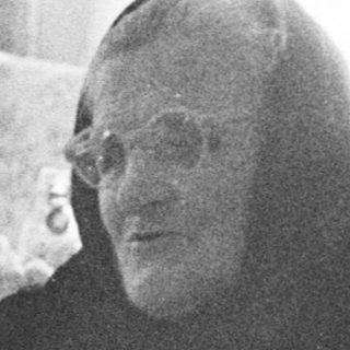 Monk conversing with people around a table indoors.