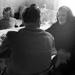 Monk conversing with people around a table indoors.
