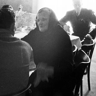 Monk conversing with people around a table indoors.
