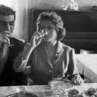 Couple drinks wine at a table with food.
