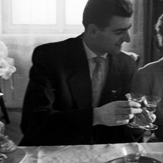 Couple seated at a table, holding drinks indoors.