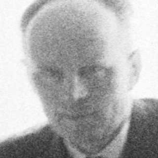 Man seated near a vintage radio, captured in black and white.