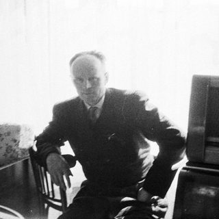 Man seated near a vintage radio, captured in black and white.