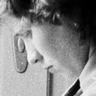 Woman seated, reading while looking down in a room.