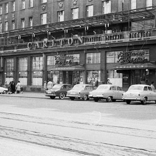 Black and white photo of a hotel with cars parked outside.