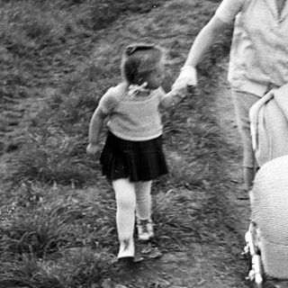 Woman walks along a path, holding a child's hand.