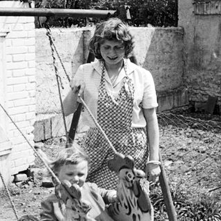 Child on a horse swing with a woman nearby.