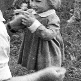 Man crouches, assisting a young girl in a grassy area.