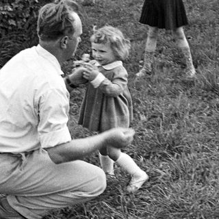 Man crouches, assisting a young girl in a grassy area.
