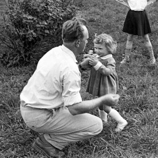 Man crouches, assisting a young girl in a grassy area.