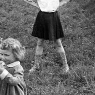 Man crouches, assisting a young girl in a grassy area.
