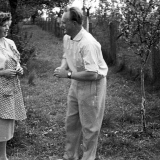 Couple standing outdoors, likely in a garden or farm setting.