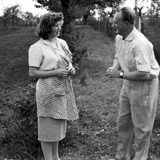 Couple standing outdoors, likely in a garden or farm setting.