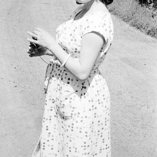 Woman in dress stands on a road, looking at camera.