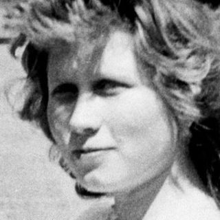 Woman in dress stands on a road, looking at camera.