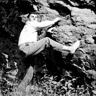 Man in trousers is jumping near a rocky hillside.