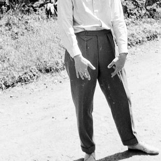 Man stands barefoot in trousers and shirt outdoors.
