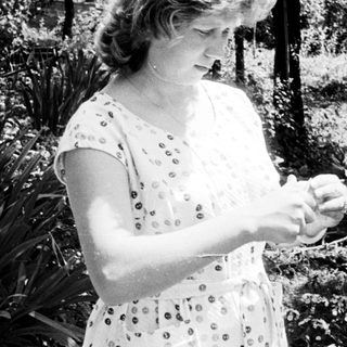 Woman in dress standing outdoors, looking down at her hands.
