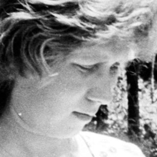Woman in dress standing outdoors, looking down at her hands.