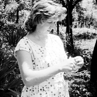 Woman in dress standing outdoors, looking down at her hands.