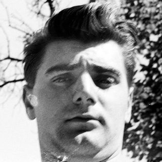 Here's a brief summary of the image: Black and white portrait of a man with slicked-back hair.