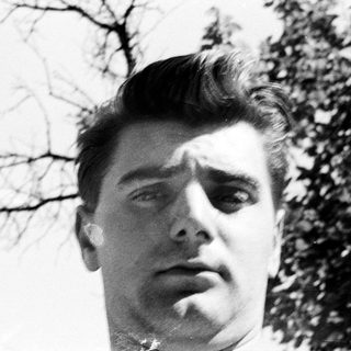 Here's a brief summary of the image: Black and white portrait of a man with slicked-back hair.