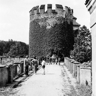 People walk along a path beside an ivy-covered tower.