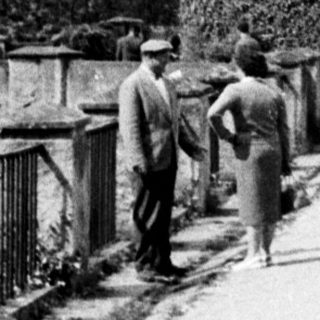 People walk along a path beside an ivy-covered tower.