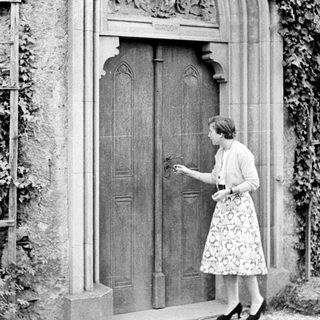Woman approaches ornate door with ivy-covered wall.