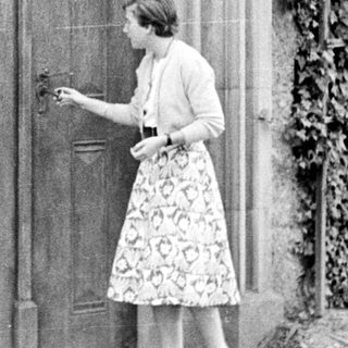 Woman approaches ornate door with ivy-covered wall.
