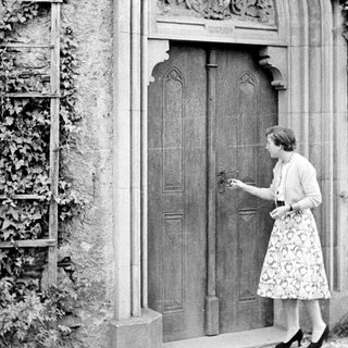 Woman approaches ornate door with ivy-covered wall.