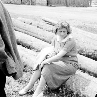 Woman sits on logs, appearing distressed, in black and white.