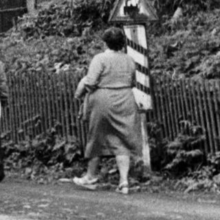 People walk past a ruined tower and a house.