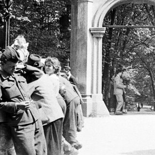 People gather near an ornate archway in a park.