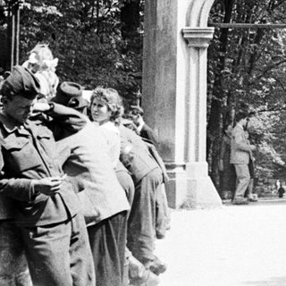 People gather near an ornate archway in a park.