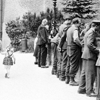 Here's a brief summary of the image: People and soldiers on a pathway near a building.