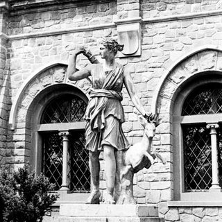 Classical statue of a woman with a deer stands on pedestal.