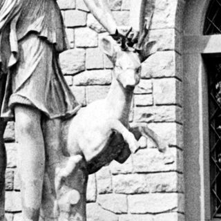 Classical statue of a woman with a deer stands on pedestal.