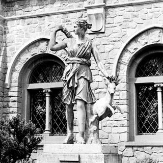 Classical statue of a woman with a deer stands on pedestal.