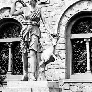 Classical statue of a woman with a deer stands on pedestal.