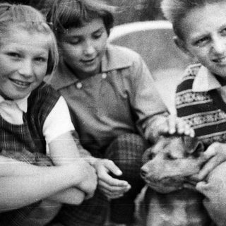 Three children holding a lamb in a black and white photo.