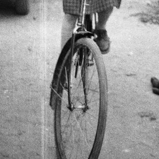 Here's a brief summary of the image: Young girl rides a bicycle near a vintage car.