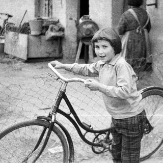 Boy stands near a bicycle, a woman in background.