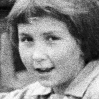 Boy stands near a bicycle, a woman in background.