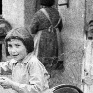Boy stands near a bicycle, a woman in background.
