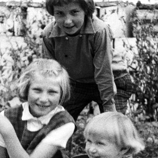Three children pose outdoors in a black and white photograph.