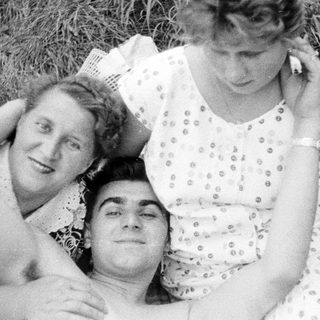 Three people relax in grass, posing for a portrait.